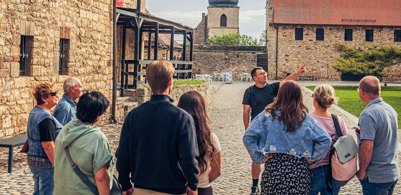 Eine Gruppe an Menschen schaut und hört einem Gästeführer zu, wie er das Gelände der Burg Querfurt zeigt.