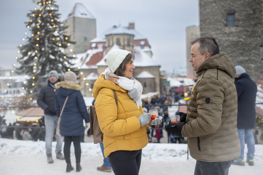 Älteres Paar unterhält auf dem winterlich verschneiten Burghof der Burg Querfurt und hält Glühweintassen in der Hand.