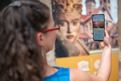 Frau hält Handy vor sich und steht vor dem Eingang des Naumburger Doms