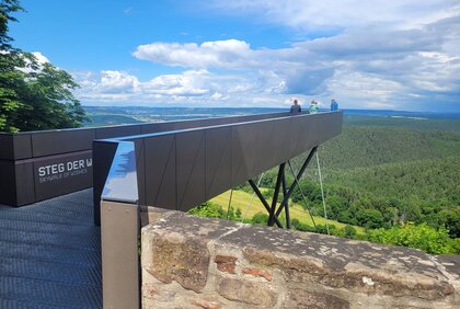 Menschen stehen auf einem modernen Skywalk, genannt Steg der Wünsche, drumherum Landschaft