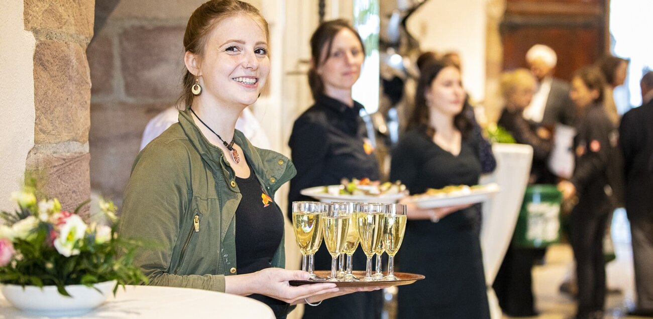 Junge Servicedame, die lächelnd ein Tablett mit Sektgläser hält.