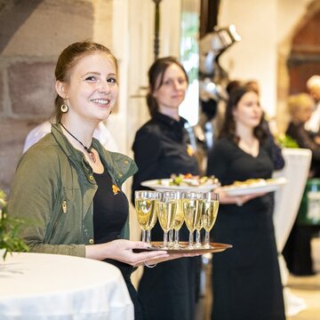 Junge Servicedame, die lächelnd ein Tablett mit Sektgläser hält.