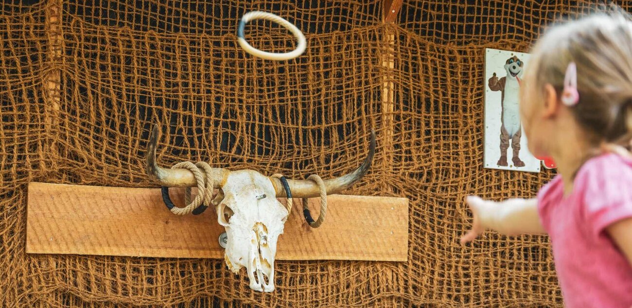 Ein kleines Mädchen wirft mit einem Ring auf ein Bullen Skelett.