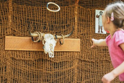 Ein kleines Mädchen wirft mit einem Ring auf ein Bullen Skelett.