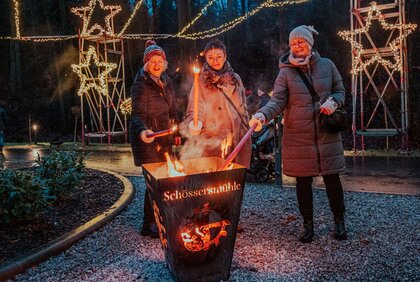 Drei Frauen entzünden am Lagerfeuer im Weihnachtstal Mühltal ein paar Fackeln