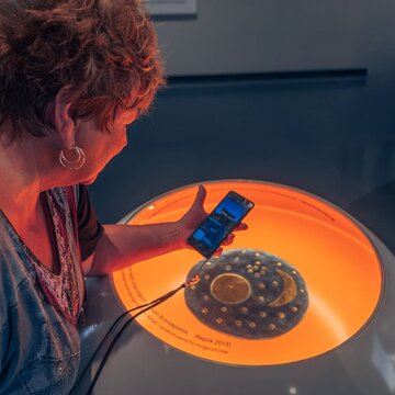 Frau schaut sich die App der Arche Nebra über einem Objekt der Ausstellung an