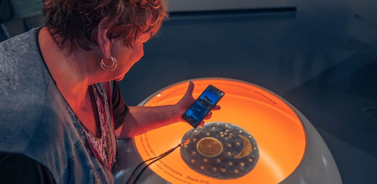 Frau schaut sich die App der Arche Nebra über einem Objekt der Ausstellung an