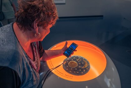 Frau schaut sich die App der Arche Nebra über einem Objekt der Ausstellung an