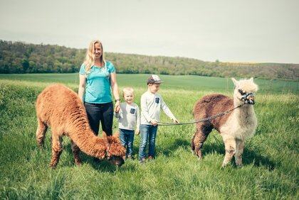 Mutter, 2 Kinder und verschiedene Alpakas auf einer Wiesse