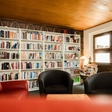 Gemütlicher Leseraum mit großen Bücherregalen, Sesseln und Holzbalkendecke, daneben Fenster mit Blick auf Fachwerkgebäude.