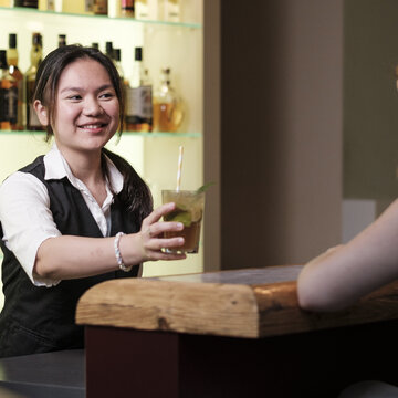 Portrait von Azubi Sydney Gunawan hinter der Bar beim Servieren eines Cocktails