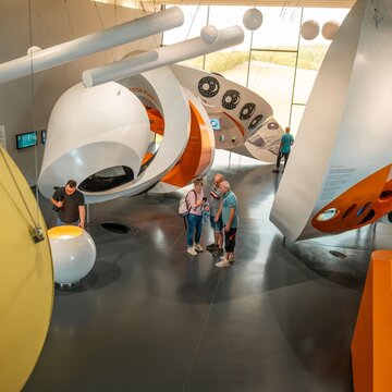 Vier Menschen besichtigen den Innenraum des Museums Arche Nebra, in dem Planeten von der Decke abhängen