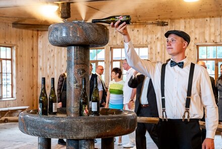 Mann gießt eine Flasche Wein in eine Zerstäbungsmaschine, oberhalb tritt feiner Weinnebel aus. Rundherum stehen Menschen und schauen zu.