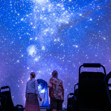 Zwei Frauen stehen im Zeiss-Planetarium Jena und schauen sich den Sternenhimmel an, der auf die Kuppel projiziert ist