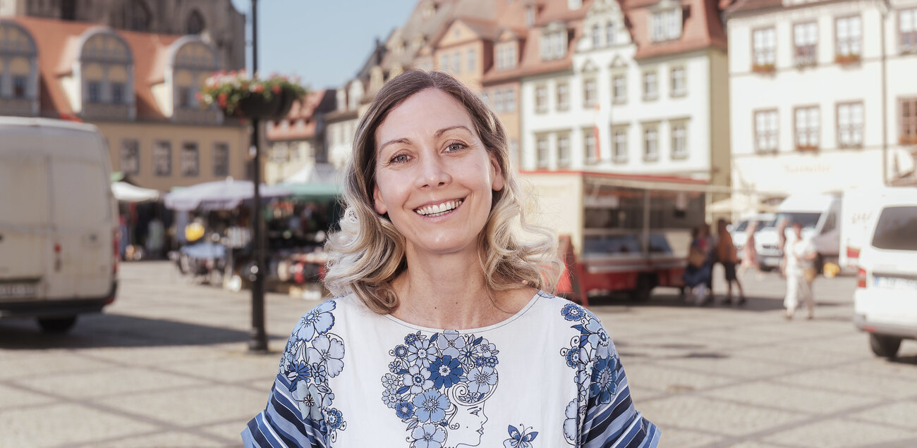 Ulrike Kappis steht auf einem Platz in einer Stadt und strahlt in die Kamera