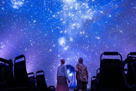Zwei Frauen stehen im Zeiss-Planetarium Jena und schauen sich den Sternenhimmel an, der auf die Kuppel projiziert ist