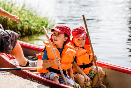 Zwei Kinder sitzen in einem Kanu auf dem Wasser.