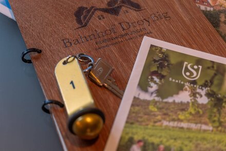 Auf einer hölzernen Mappe liegt ein Zimmerschlüssel mit der Nummer eins und ein Prospekt