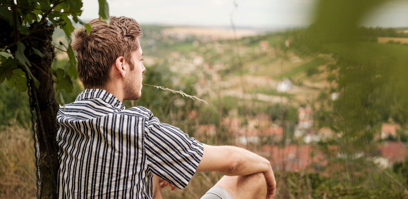 Junger Mann lehnt an Weinrebe