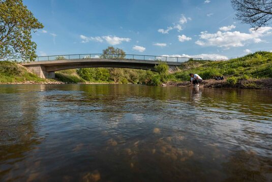 Frau am Ufer der Weißen Elster mit darüberliegender Brücke bei Haynsburg