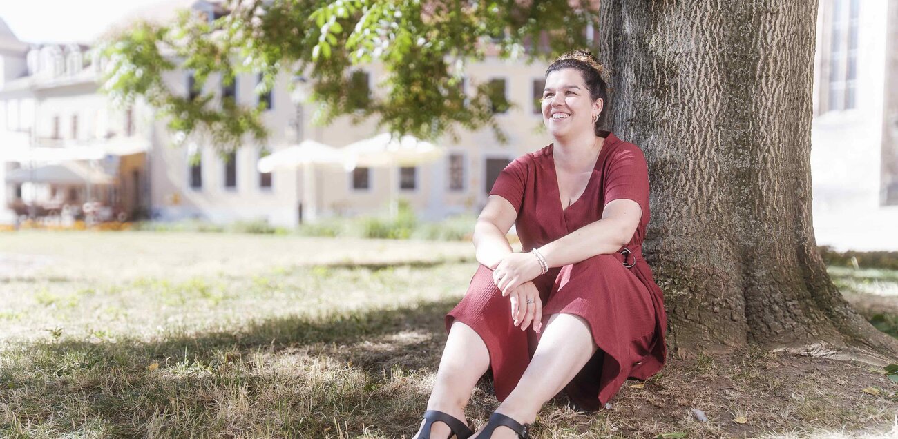Nadine Rosenberg sitzt lachend angelehnt an einen Baum.