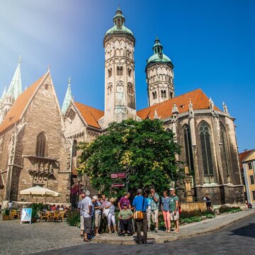 Eine Gruppe steht vor dem Naumburger Dom und hört einem Gästeführer zu