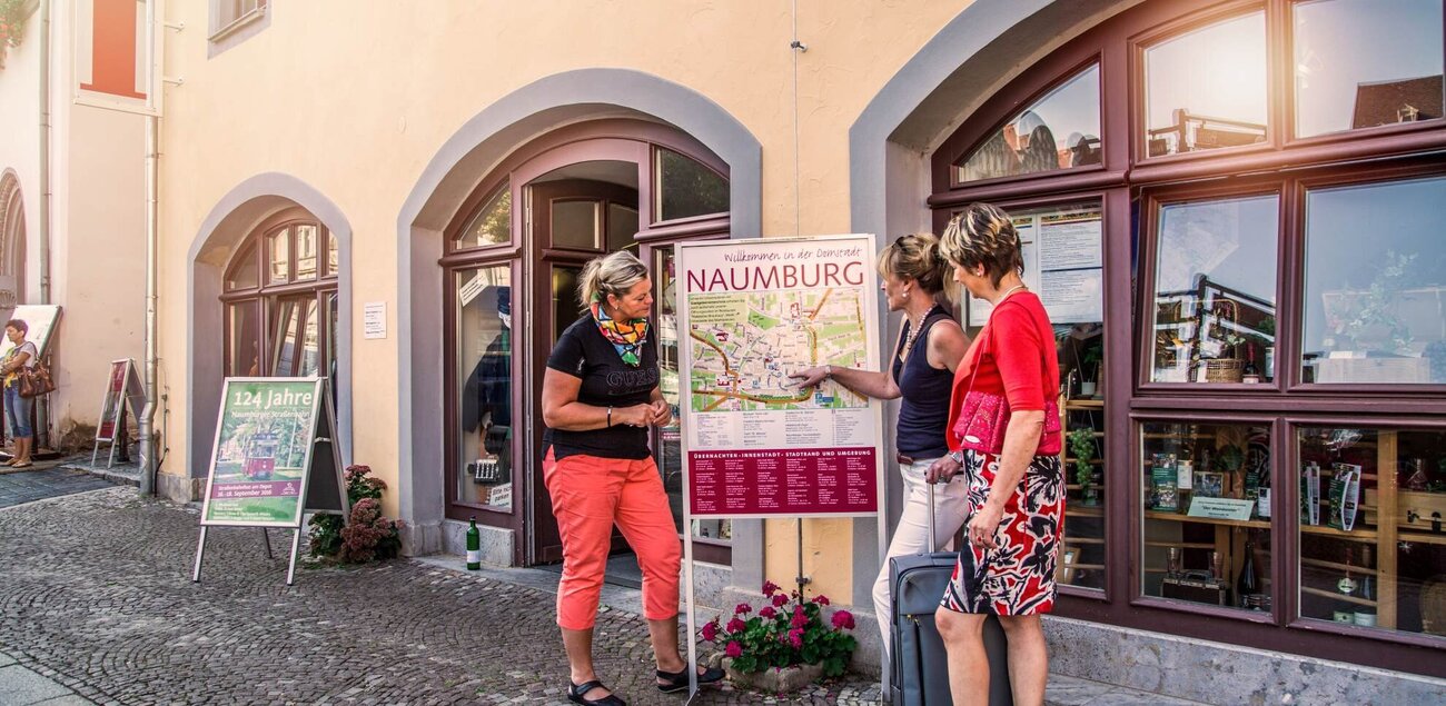 Zwei Frauen lassen sich von einer Mitarbeiterin der Tourist-Information Naumburg den Weg auf einer Karte zeigen.