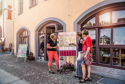Zwei Frauen lassen sich von einer Mitarbeiterin der Tourist-Information Naumburg den Weg auf einer Karte zeigen.