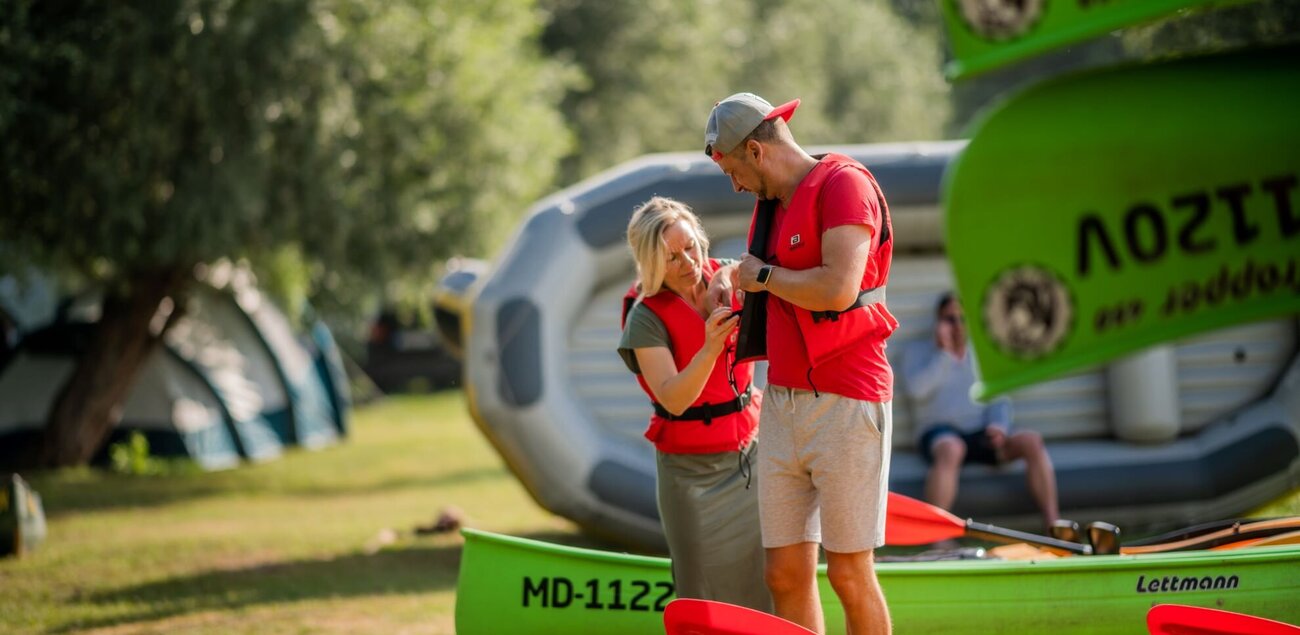 Frau hilft Mann beim Anlegen der Schwimmweste vor dem Schlauchbootausflug