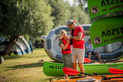 Frau hilft Mann beim Anlegen der Schwimmweste vor dem Schlauchbootausflug