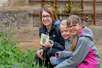 Zwei Kinder und eine Frau zeigen ihr Bastelergebnis im Ferienprojekt "Düfte des Mittelalters" in der KinderDomBauhütte am Naumburger Dom