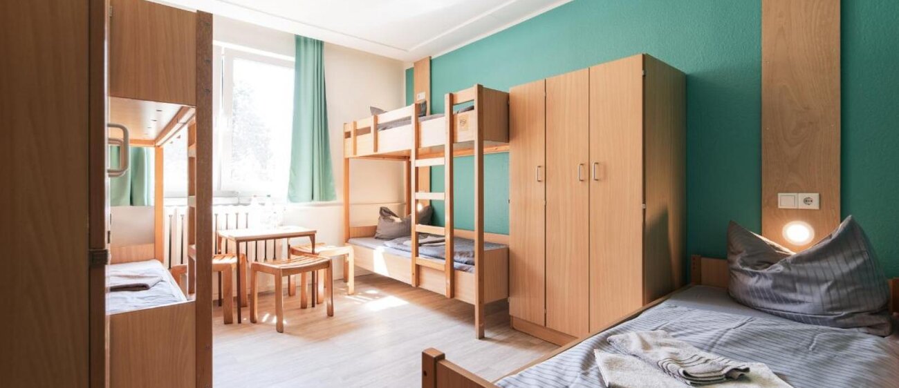 Zimmer der Jugendherberge Nebra mit Einzelbett, Doppelstockbett, Tisch mit Stühlen und Kleiderschrank