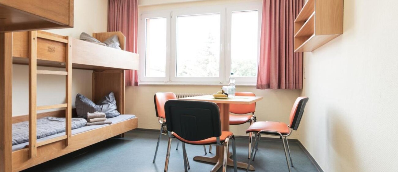Zimmer der Jugendherberge mit Doppelstockbetten und Tisch mit vier Stühlen