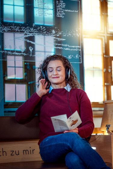Junge Frau sitzt auf der Hörbank im Heinrich-Schütz-Haus Weißenfels und genießt die Musik