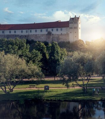 Burg Wettin im Sonnenaufgang oberhalb der Saale mit Saalewiesen und zwei Radfahrenden
