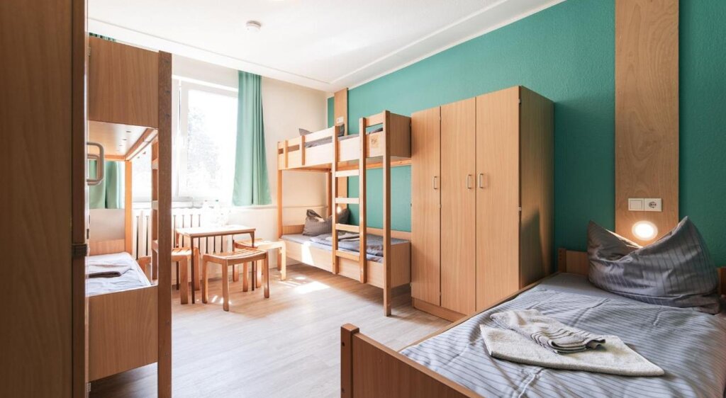 Zimmer der Jugendherberge Nebra mit Einzelbett, Doppelstockbett, Tisch mit Stühlen und Kleiderschrank