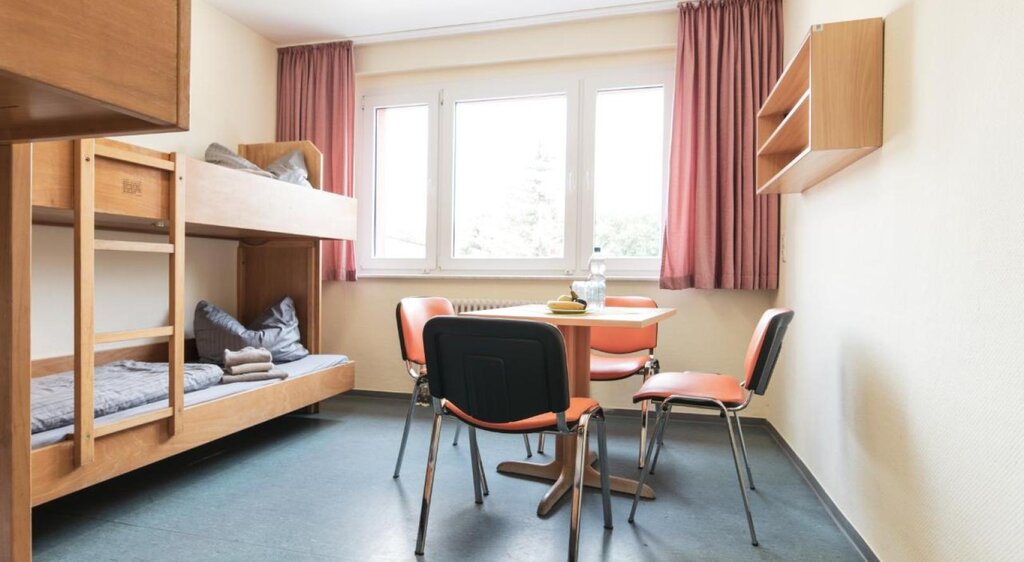 Zimmer der Jugendherberge mit Doppelstockbetten und Tisch mit vier Stühlen
