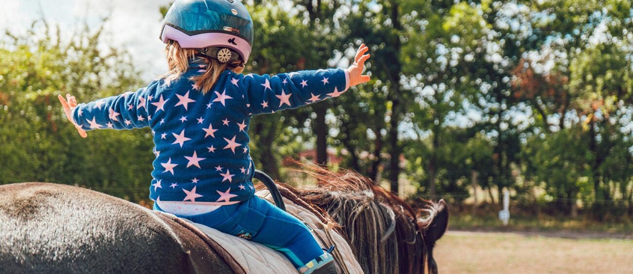 Kind reitet auf einem Pferd.